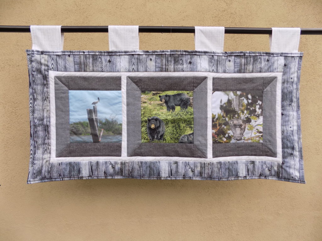 photo of hanging quilt with images of a brown pelican, black bear, and alligator
