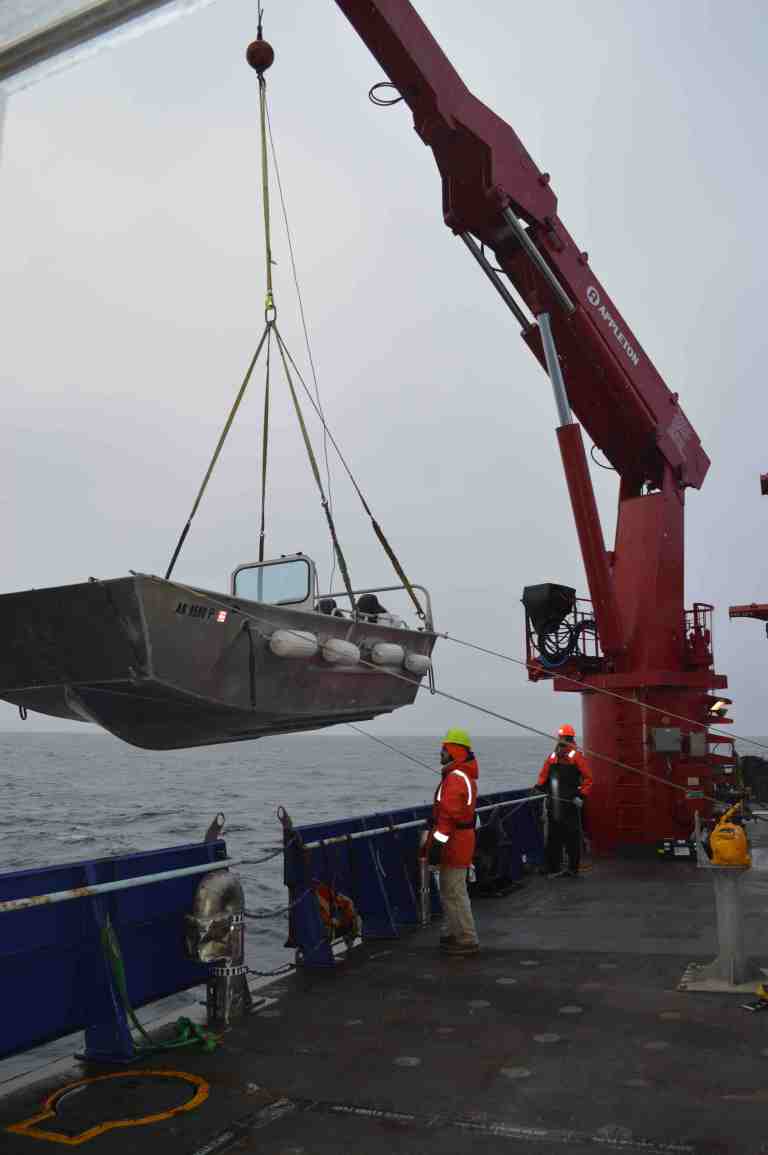 The crew uses a crane to lower a small boat over the side of the ship to deploy the glider away from the ship.