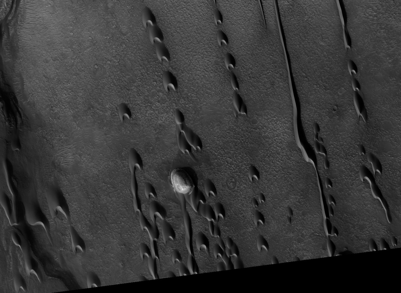 Barchan dunes march across a plain in the Hellespontus region west of Hellas basin on Mars. The orientation of their horns indicates consistent winds out of the east, blowing right to left in this image captured by the Mars Reconnaissance Orbiter. Sunshine lights the steep slopes of the leeward, or downwind, faces, on the dunes’ left sides. The dunes migrate with the wind, sometimes merging or extending long fingers that spawn new dunes. Credit: NASA/JPL/University of Arizona