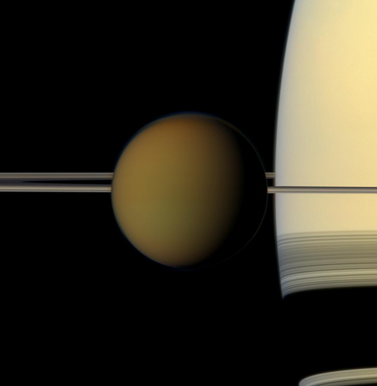 Hazy, orange Titan, Saturn's largest moon, passes in front of the planet and its rings in this tru-color image from Casssini. Credit: NASA