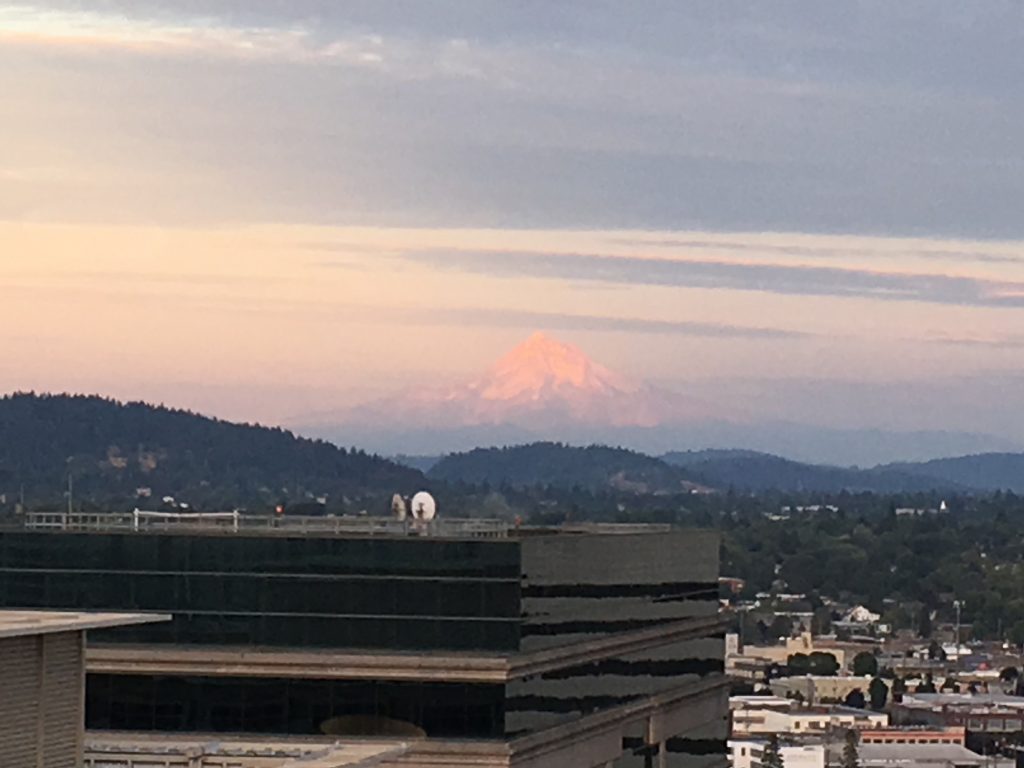 A sunset-lit Mount Hood volcano viewed from a high-rise in downtown Portland, Oregon