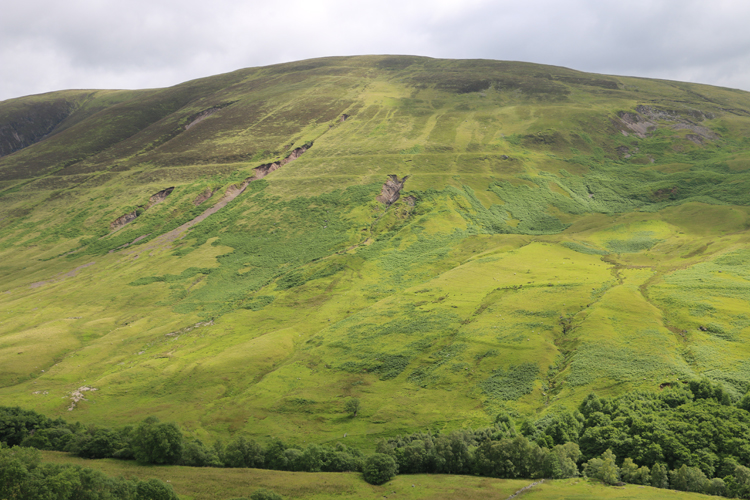 Photograph showing bare gullies cutting into the Glen Roy hillside, eating away at both the vegetation and the continuity of the horizontal "Roads" etched into the hill.