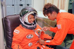 NASA astronaut Mae Jemison waits as her suit technician, Sharon McDougle, performs an unpressurized and pressurized leak check on her spacesuit at the Operations and Checkout Building at Kennedy Space Center in Florida. Photo Credit: NASA